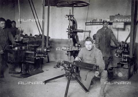 AVQ-A-000006-0014 - View of the workshop of the 9° Machinegun Division near Noventa Vicentina. In the foreground a young soldier is working on a machinegun. Behind him a few machines maneuvered by soldiers - Date of photography: 1918-1919 - Alinari Archives, Florence