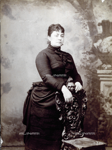 FBQ-F-000039-0000 - Studio portrait of a young woman against a painted backdrop. She is leaning against an inlaid chair and wearing elaborate late nineteenth century dress - Date of photography: 1885 ca. - Alinari Archives, Florence