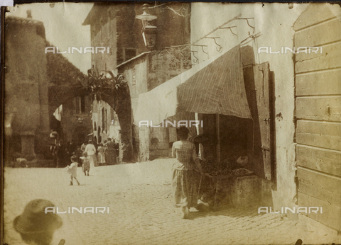 FBQ-F-001210-0000 - A square in Tivoli. In the foreground, a shop with merchandise on view outside and a woman seen from the back. In the background, a lane with numerous pedestrians - Date of photography: 1882 -1887 ca. - Alinari Archives, Florence