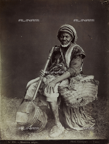 FBQ-F-001502-0000 - Full-length portrait of an elderly black musician in humble ethnic attire. He is wearing a straw bag around his neck and with his right hand is holding a typical string instrument - Date of photography: 1860 -1870 - Alinari Archives, Florence