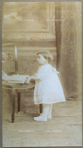 FBQ-F-002231-0000 - Full-length portrait, in profile of Teresa Spinola Maggi. The little girl is wearing an elegant dress. She is standing in front of a chair on which an open book is placed - Date of photography: 1900 - 1910 - Alinari Archives, Florence