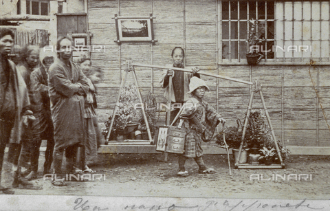 FBQ-S-001734-0019 - A group of people posing for the camera, along a road in Japan. At the center of the picture is a dwarf, with a female figure behind him, holding a mobile bamboo structure for transporting flower pots - Date of photography: 1870 ca. - Alinari Archives, Florence