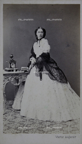 IMA-F-644114-0000 - Lady in white dress with dark stole, on the Atelier table a clock and photo albums, full figure - Date of photography: 1867 - Victor Angerer / Austrian Archives / brandstaetter images /Alinari Archives