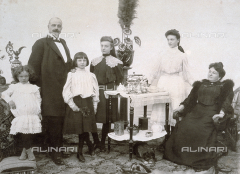 MFC-F-000107-0000 - Family portrait composed of four daughters of different ages and their parents. The group is gathered around a small table on which there are various tea-pots and a complete tea service. A small dog is curled up under the table - Date of photography: 1907 - Alinari Archives, Florence