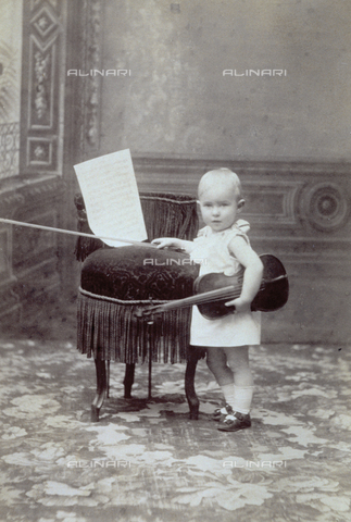 MFC-F-001052-0000 - Full-length portrait of a little girl beside a small armchair on which some sheet music is placed. She is holding a violin under her arm - Date of photography: 1880-1900 ca. - Alinari Archives, Florence