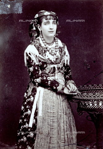 MFC-F-001362-0000 - Three-quarter-length portrait of a woman in traditional dress. She is wearing a flowered dress, a fringed shawl, an apron, necklaces and a kerchief on her head - Date of photography: 1880-1900 ca. - Alinari Archives, Florence