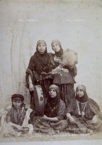 MFC-F-001426-0000 - Portrait of two young egyptian women in traditional clothes. Three women are sitting on the ground, another two are standing and are holding tambourines - Date of photography: 1880-1890 ca. - Alinari Archives, Florence