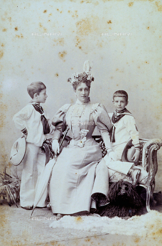MFC-F-001500-0000 - Full-length portrait of a young mother with two children in sailor outfits. The woman, elegantly dressed, is sitting on a sofa between the two children. Next to her is an umbrella, while a dog can be seen under the sofa - Date of photography: 1880-1900 ca. - Alinari Archives, Florence