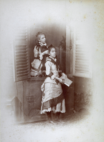 MFC-F-001725-0000 - Portrait of two girls. One is looking out a window and dressing the hair of the other girl who is standing before the window holding a book - Date of photography: 1870-1880 ca. - Alinari Archives, Florence