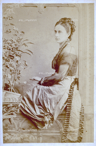MFC-F-001900-0000 - Portrait of a young woman seated at a dummy window surrounded by ornamental plants. She is holding a book - Date of photography: 1865-1871 ca. - Alinari Archives, Florence
