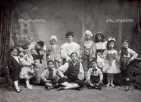MFC-F-002271-0000 - Portrait of a large group of children in costume. One girl is dressed in japanese style, others wear eighteenth century dress with wigs. Still others are dressed as musicians, with folk costumes. Three are shown seated on floor, the others standing. Behind them a painted backdrop - Date of photography: 1900 ca. - Alinari Archives, Florence