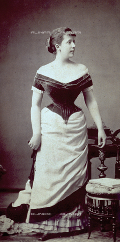 MFC-F-002326-0000 - Ritratto di giovane donna, a figura intera, in abiti da giorno. Su una sedia dello studio è posato un libro aperto - Data dello scatto: 1870-1880 - Archivi Alinari, Firenze