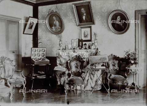 MFC-F-002334-0000 - Interior of a home furnished with armchairs, small tables, books, piece of furniture with picture frames and pictures hung on the walls - Date of photography: 1890-1900 ca. - Alinari Archives, Florence