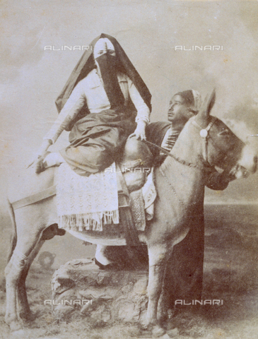 MFC-S-001133-0001 - Portrait of an arab woman in traditional attire. She is getting off a mule helped by a servant. It was surely taken in a Cairo studio - Date of photography: 1880-1890 - Alinari Archives, Florence