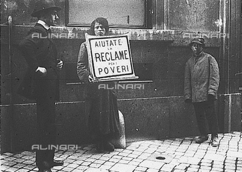 PAS-F-000299-0000 - Una donna sorregge un cartello con scritto:"Aiutate la reclame per i poveri" - Data dello scatto: 1921 - Istituto Luce/Gestione Archivi Alinari, Firenze