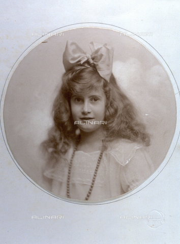 PDC-F-000593-0000 - Half-length portrait of a young girl with hair hanging down on her shoulders with a large flower on the top of her head. She is wearing a light colored dress and a necklace. She is slightly smiing and is looking toweds the camera - Date of photography: 1900-1920 - Alinari Archives, Florence