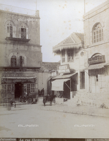 PDC-S-000752-0024 - Christian road, enclosed by buildings, in Jerusalem. A few people are sitting on a step. A horse is tied to a railing - Date of photography: 1880-1900 - Alinari Archives, Florence