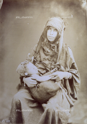 PDC-S-004348-0003 - Three-quarter length portrait of a young Egyptian woman in mModest ethnic costume holding her child. The baby lies inside a rudimentary cloth pouch hung from his mother's head - Date of photography: 1870 - 1880 ca. - Alinari Archives, Florence