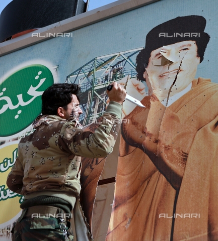 RNA-F-875719-0000 - Libyan opposition supporter uses knife to cut a poster of Muammar Gaddafi in the captured rebel town of Ras Lanuf in the east of the country - Date of photography: 05/03/2011 - Andrey Stenin / Sputnik/ Alinari Archives